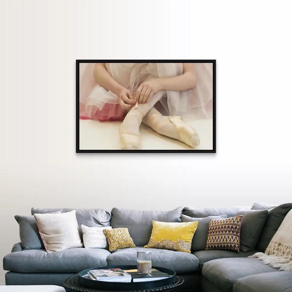 "A ballerina sitting on the floor tying her ballet shoes" Black Float Frame Canvas Art